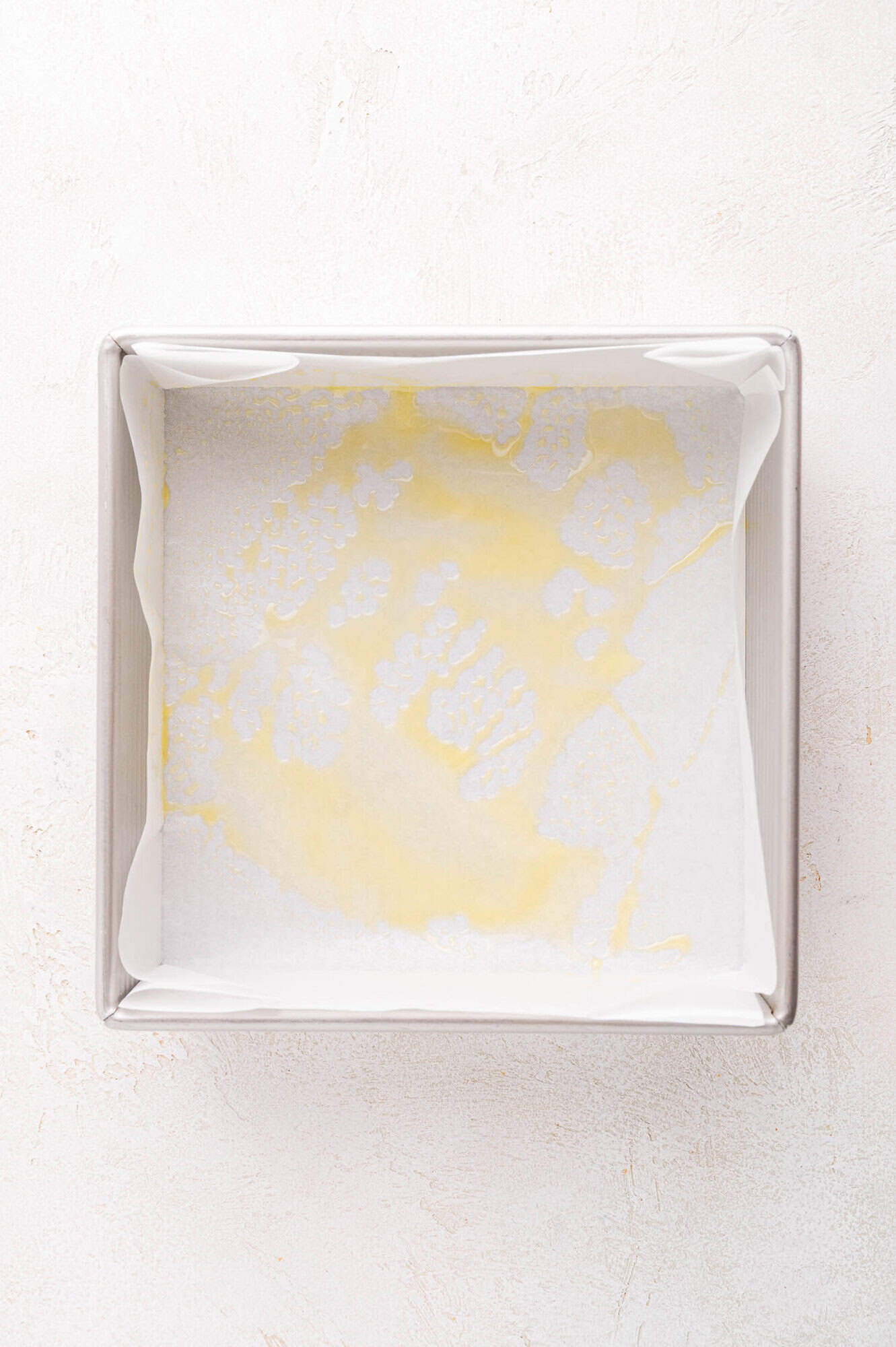 A square baking pan lined with parchment paper and lightly coated with oil, viewed from above on a light surface.