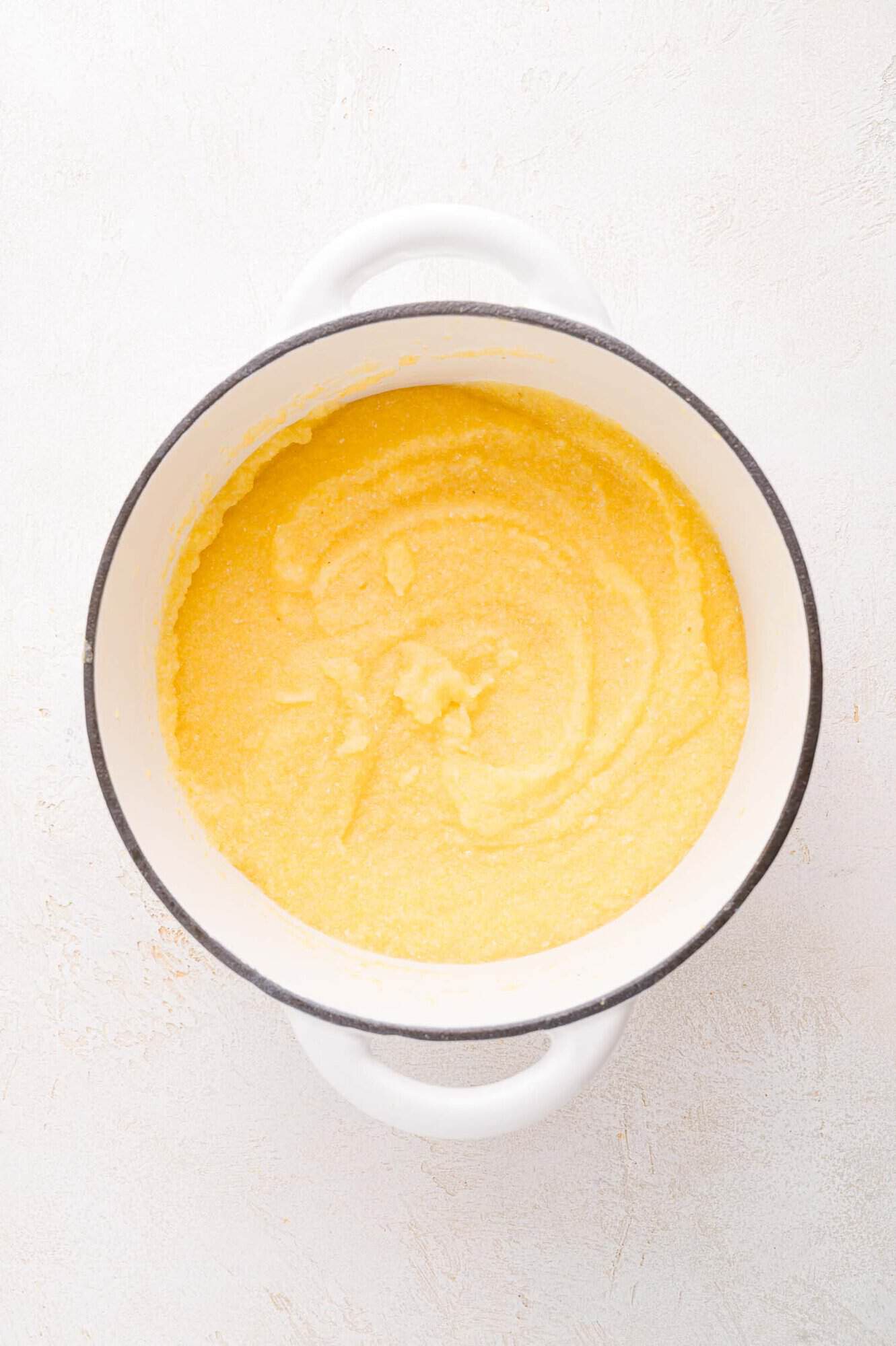 A white pot filled with cooked yellow polenta on a light, textured surface.