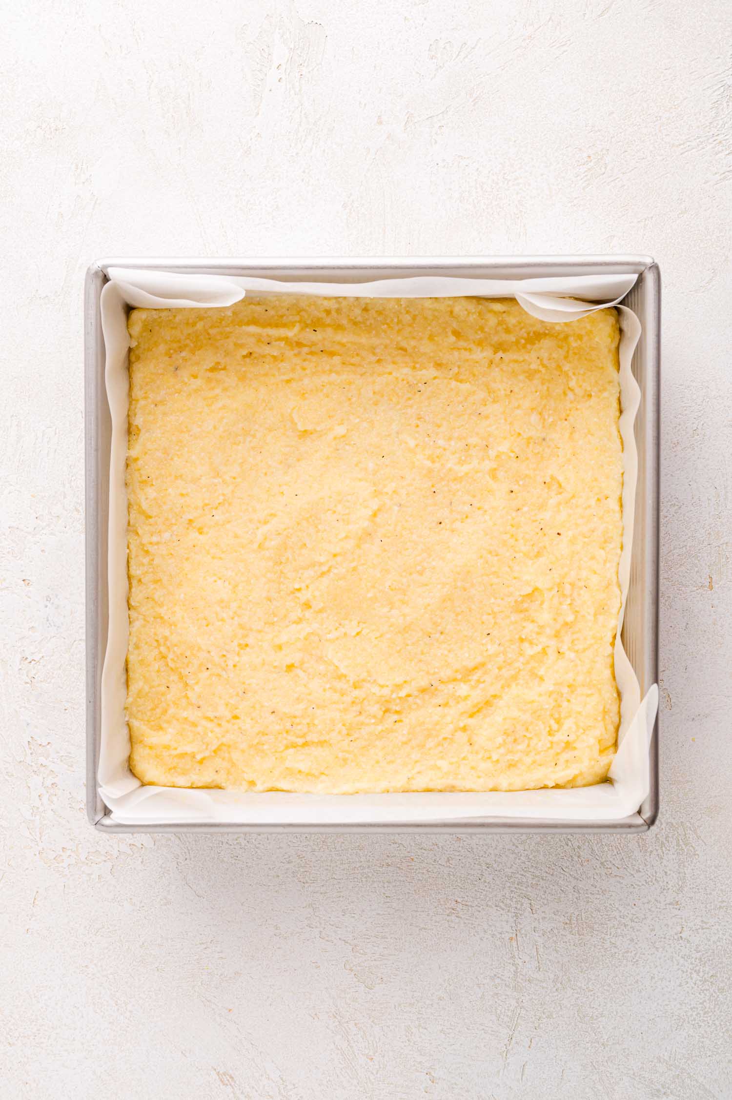 A square baking pan lined with parchment paper, filled with an even layer of polenta.