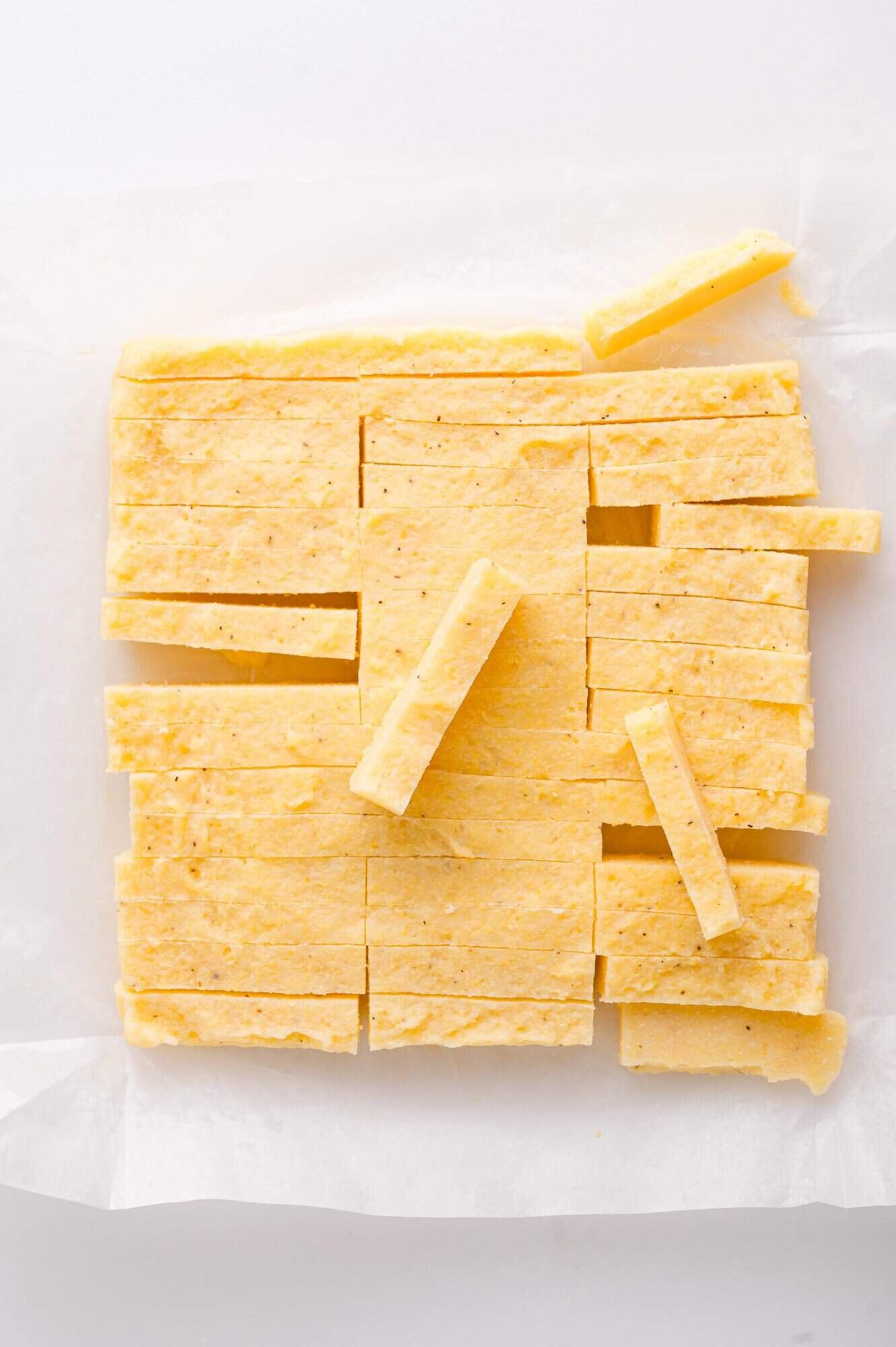 Rectangular pieces of yellow polenta are cut and stacked on parchment paper against a white background.