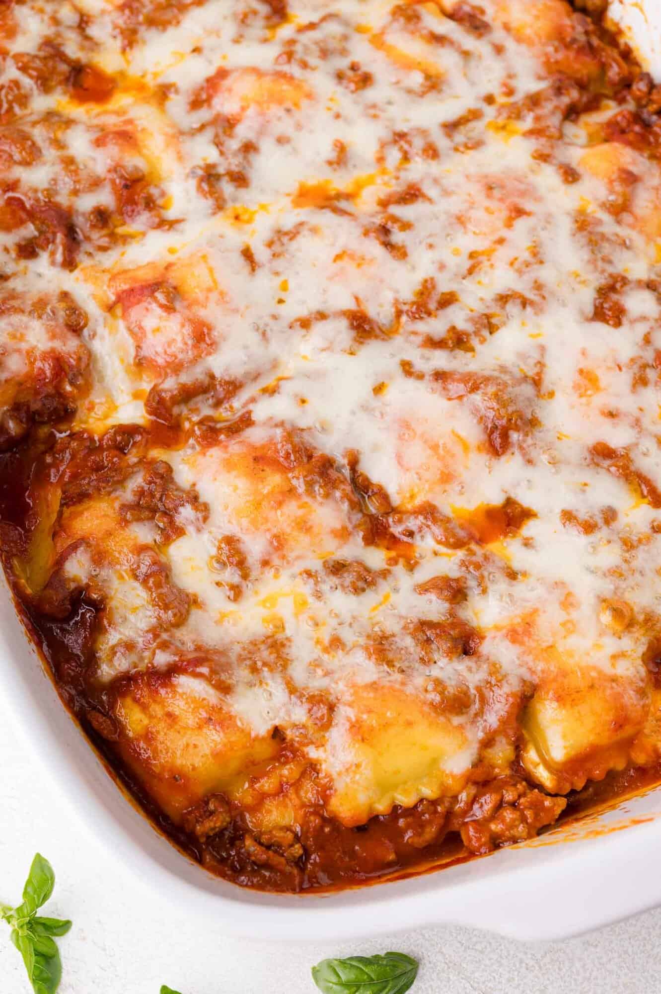 A close-up of baked ravioli in a white dish, topped with melted cheese and visible layers of meat sauce and pasta.