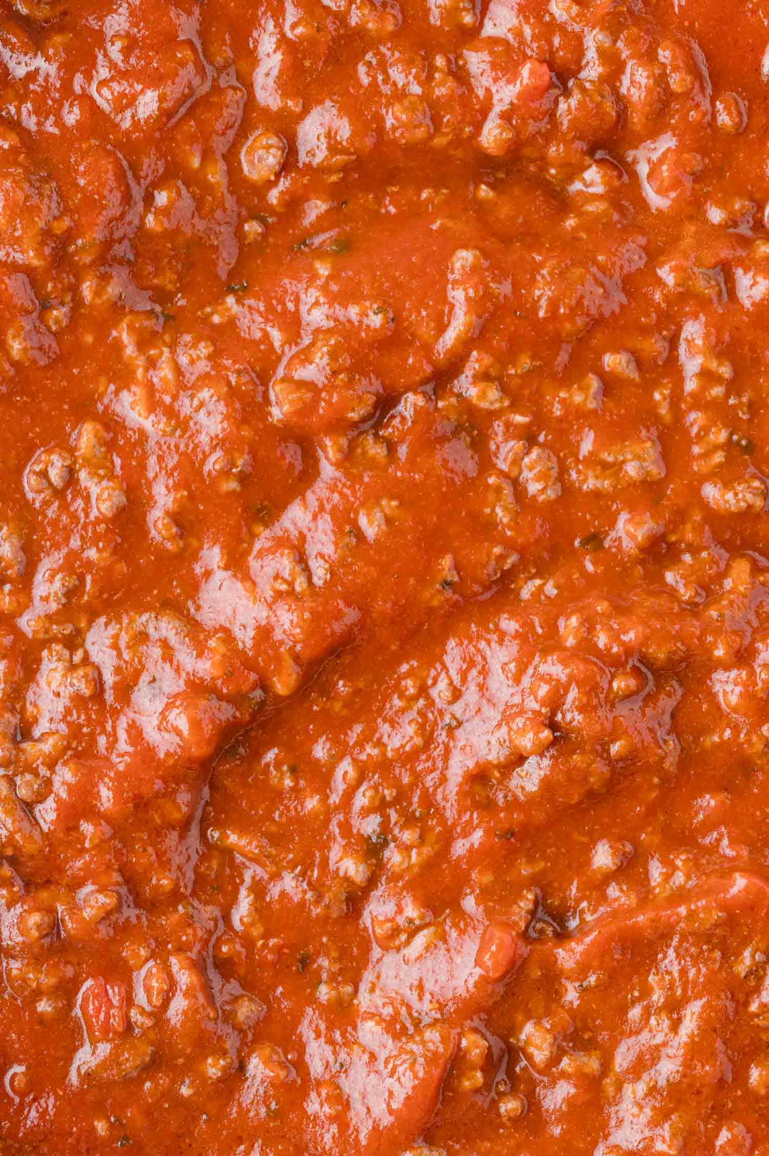 Close-up of thick, chunky red tomato sauce with visible pieces of ground meat and herbs.