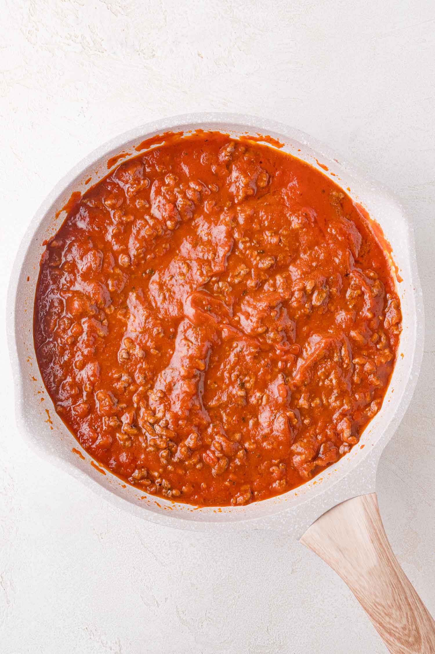 A white pan filled with a classic meat sauce, sits on a light-colored surface.