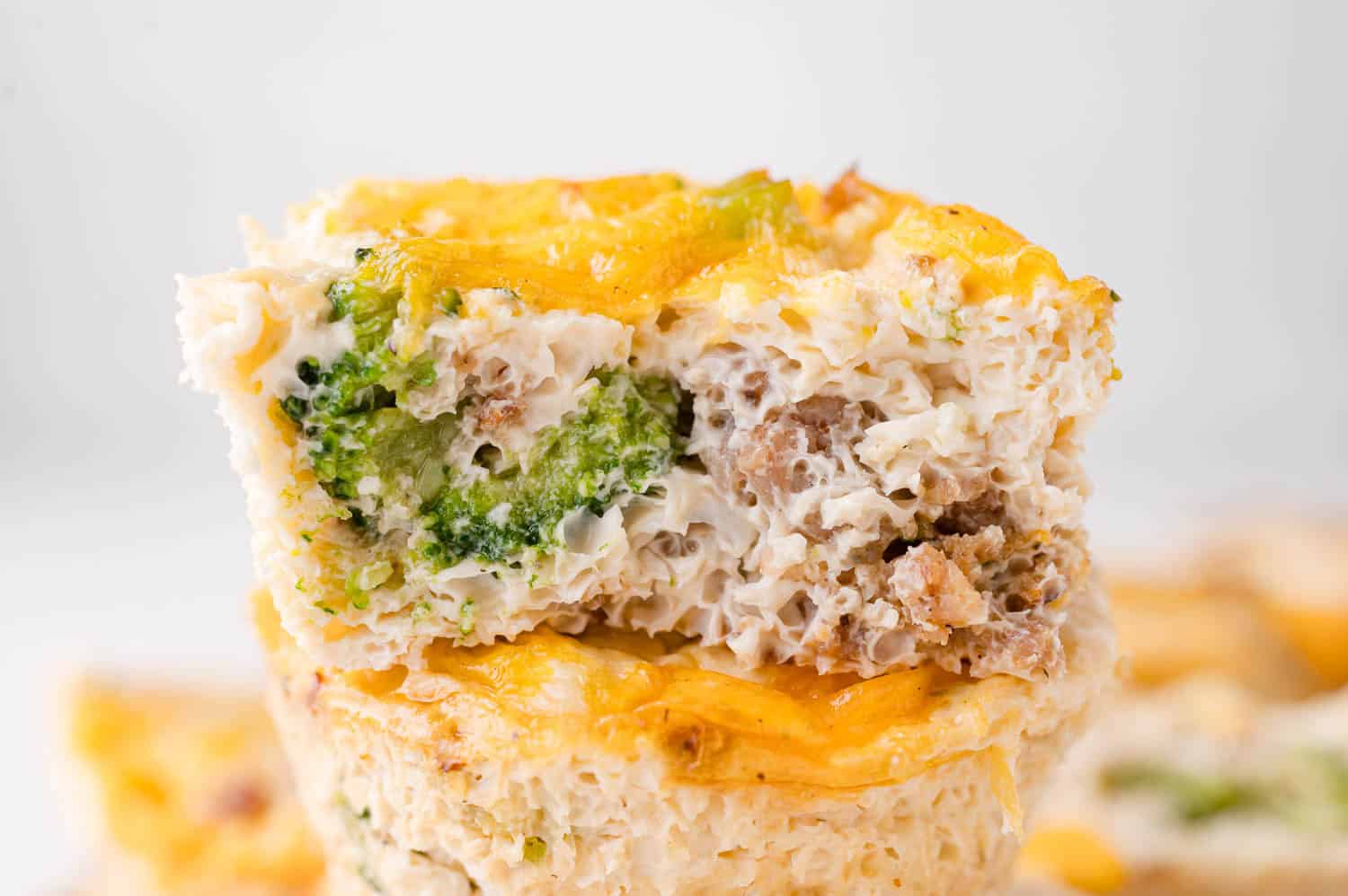 A close-up of a baked egg muffin with visible broccoli, sausage, and cheese, showing its moist texture and layers.