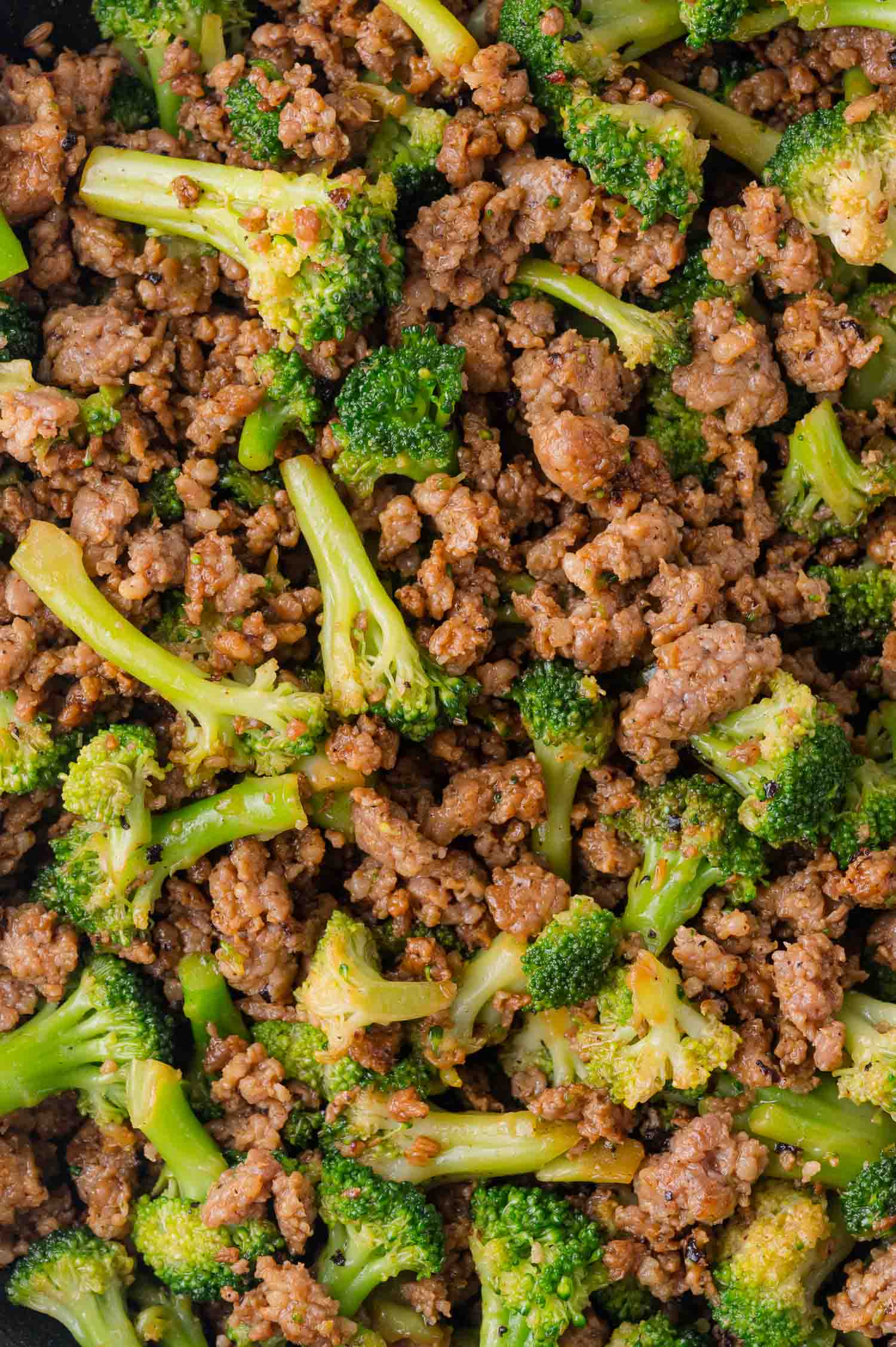 Cooked ground sausage mixed with broccoli florets, seasoned and served in a skillet.