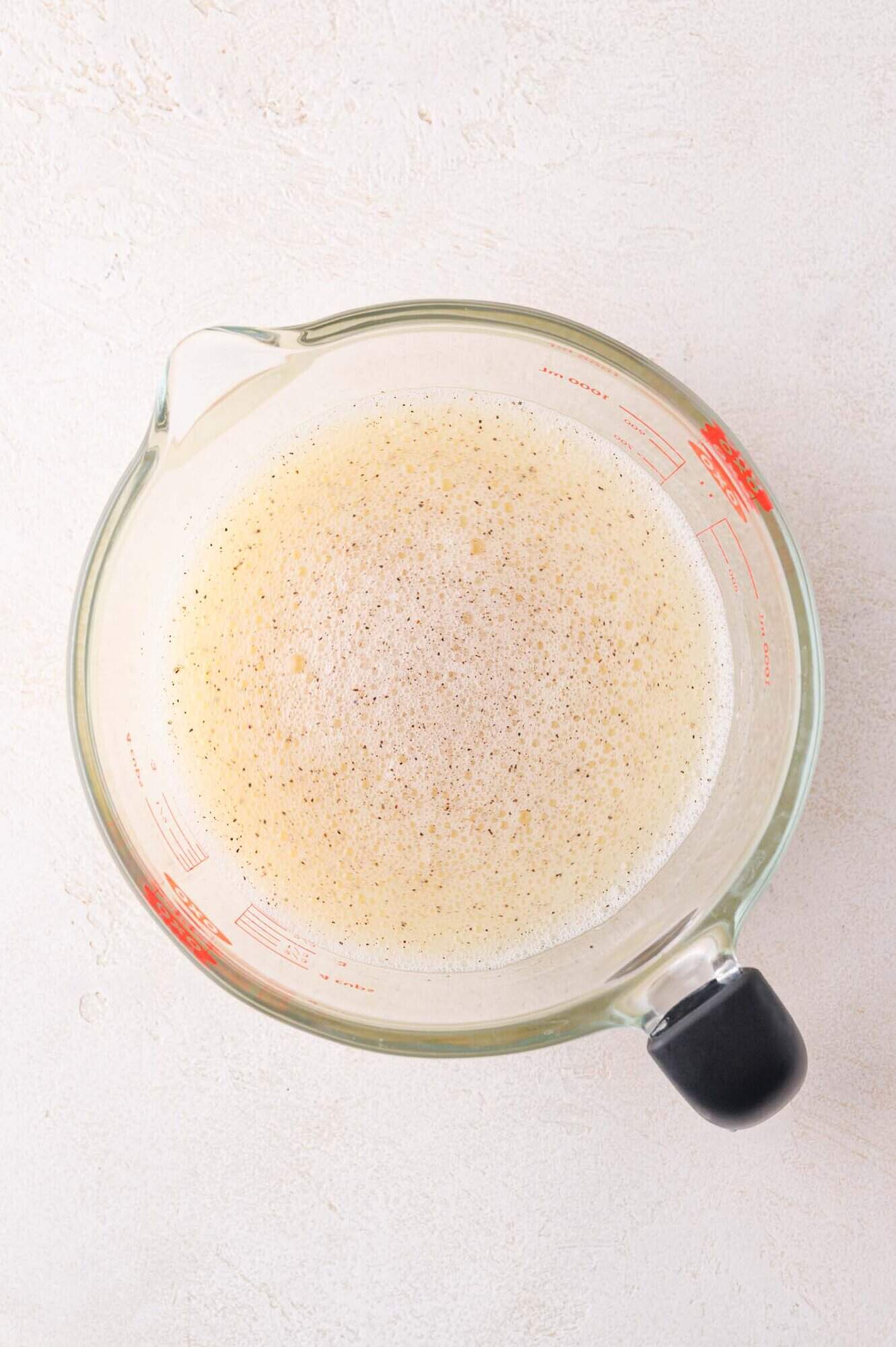 A glass measuring cup filled with whisked eggs on a white textured surface.