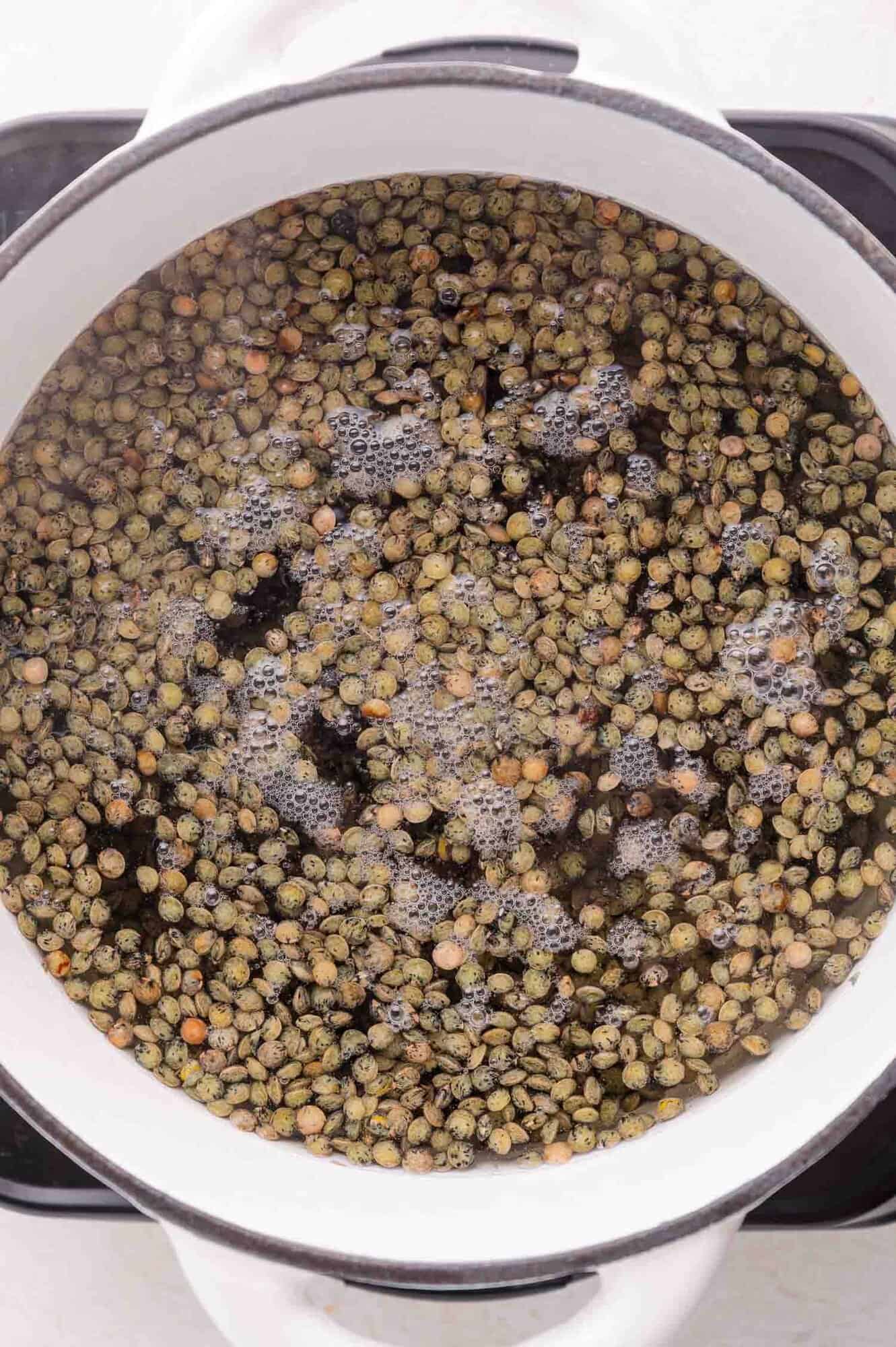 A white pot filled with green lentils submerged in water, shown from above.
