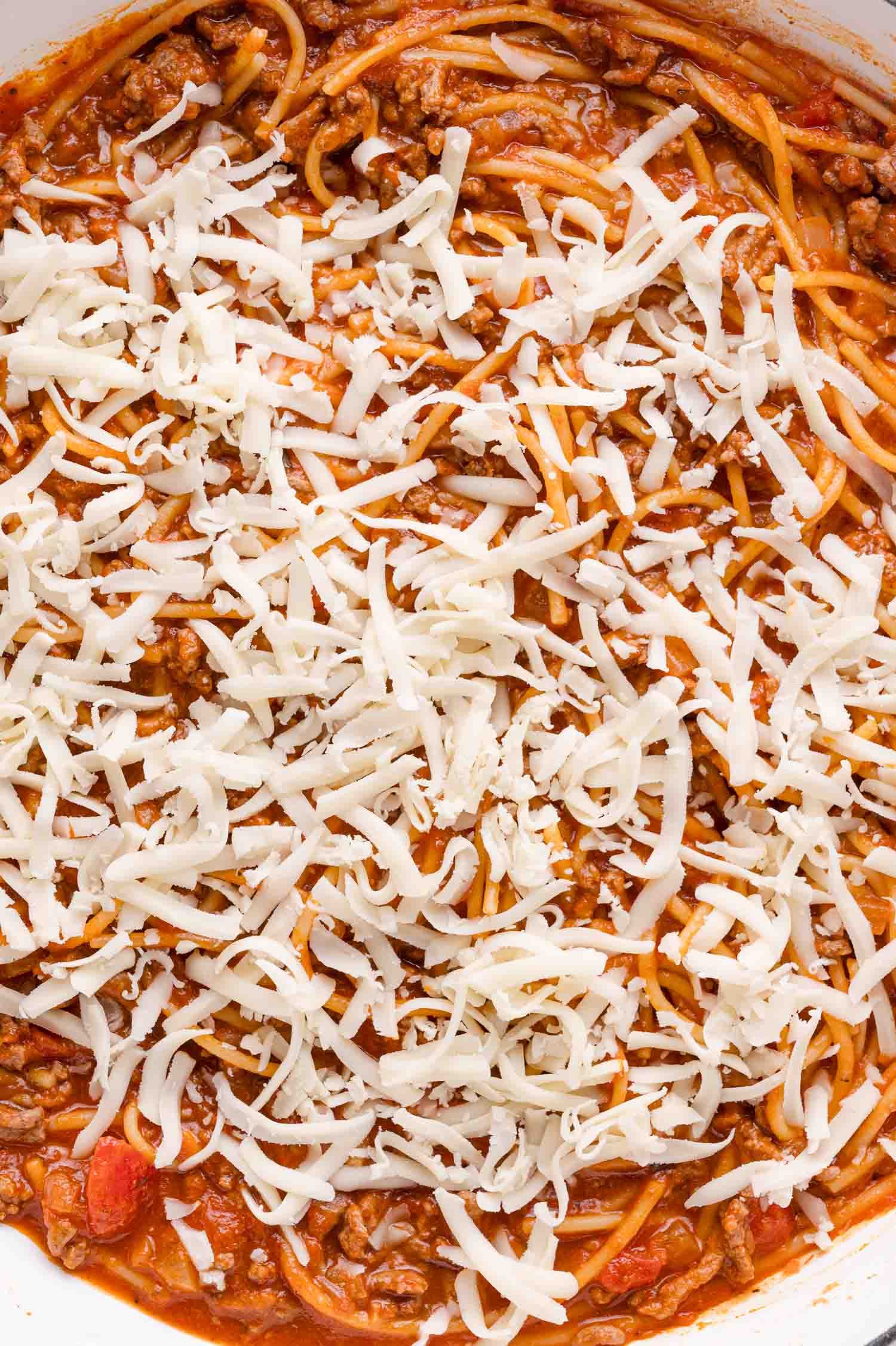 Cooked spaghetti mixed with ground beef and tomato sauce, topped with a layer of shredded mozzarella cheese.