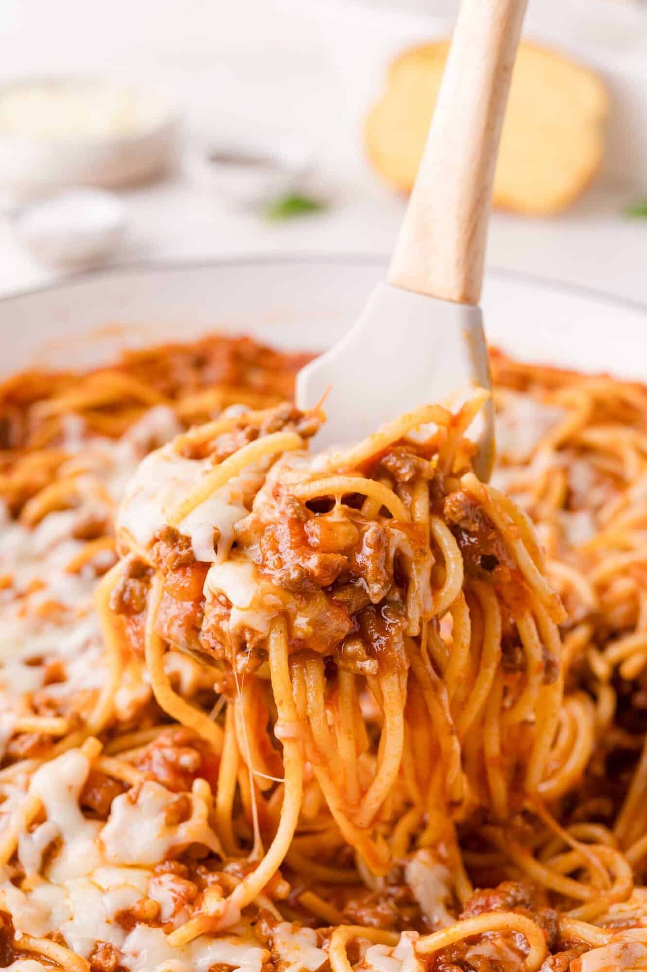 A white spatula lifts a serving of one pan spaghetti with ground meat sauce and melted cheese from a pan.