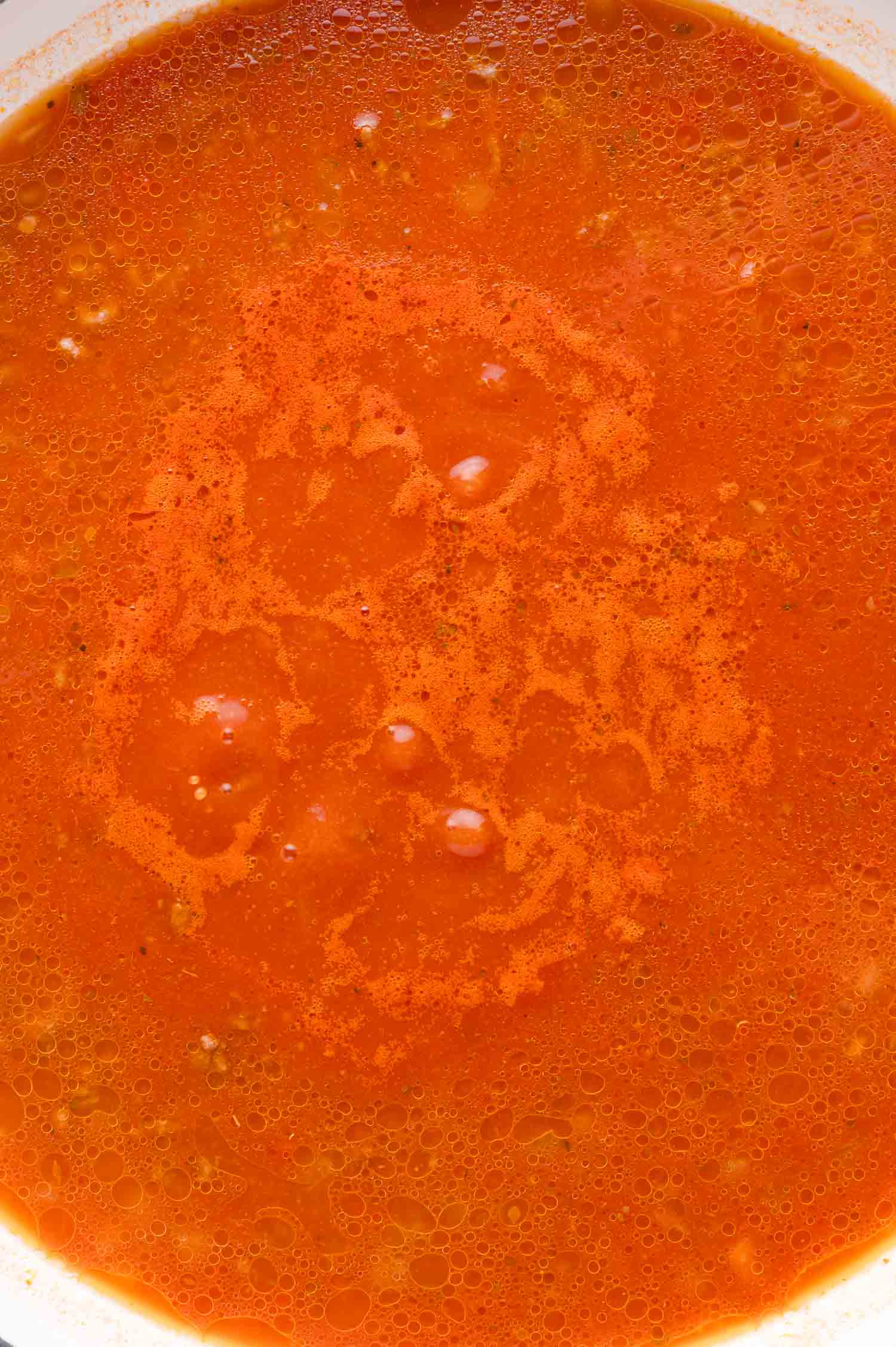 Close-up of a bowl filled with red tomato sauce, showing an oily surface and a few small bubbles.