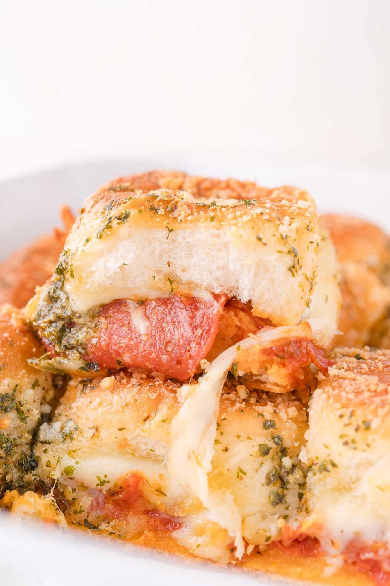 A close-up of baked pizza slider filled with melted cheese and pepperoni, topped with herbs and grated parmesan.