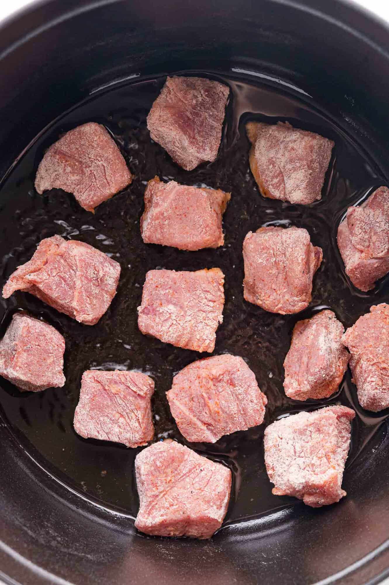 Raw beef cubes arranged in a single layer inside a black pot with a small amount of oil at the bottom.