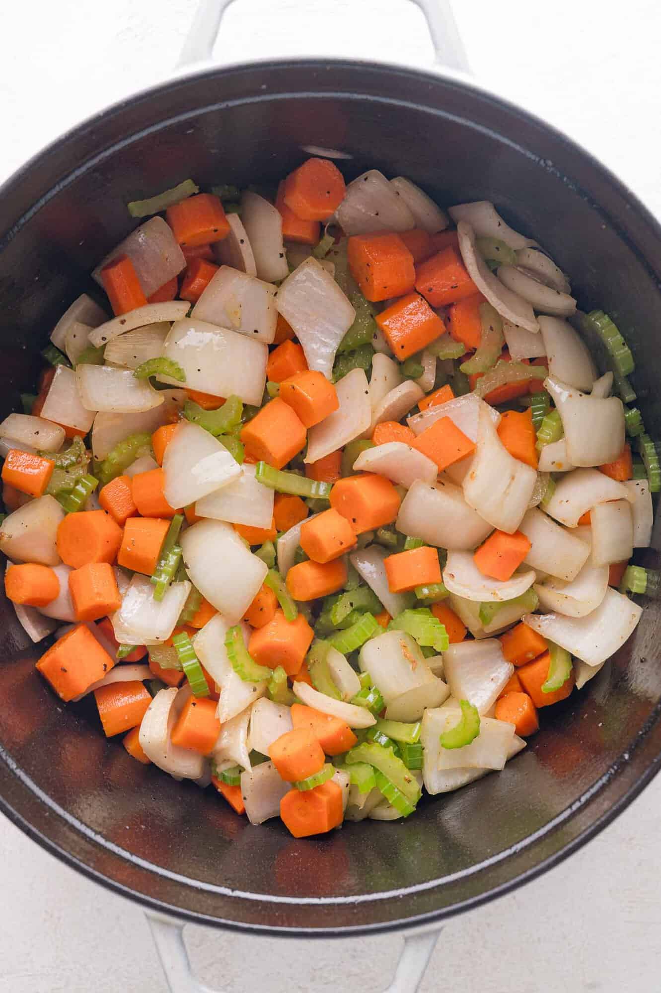 Chopped carrots, celery, and onions sautéing in a black pot.