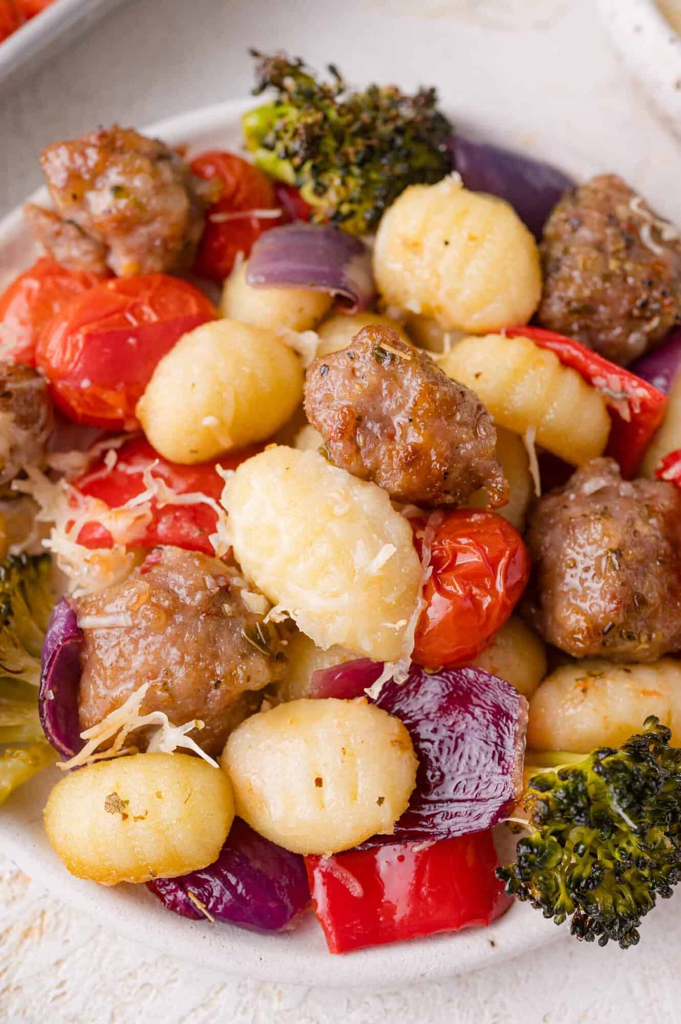 A plate of gnocchi with sausage, cherry tomatoes, red onion, red peppers, broccoli, and grated cheese.