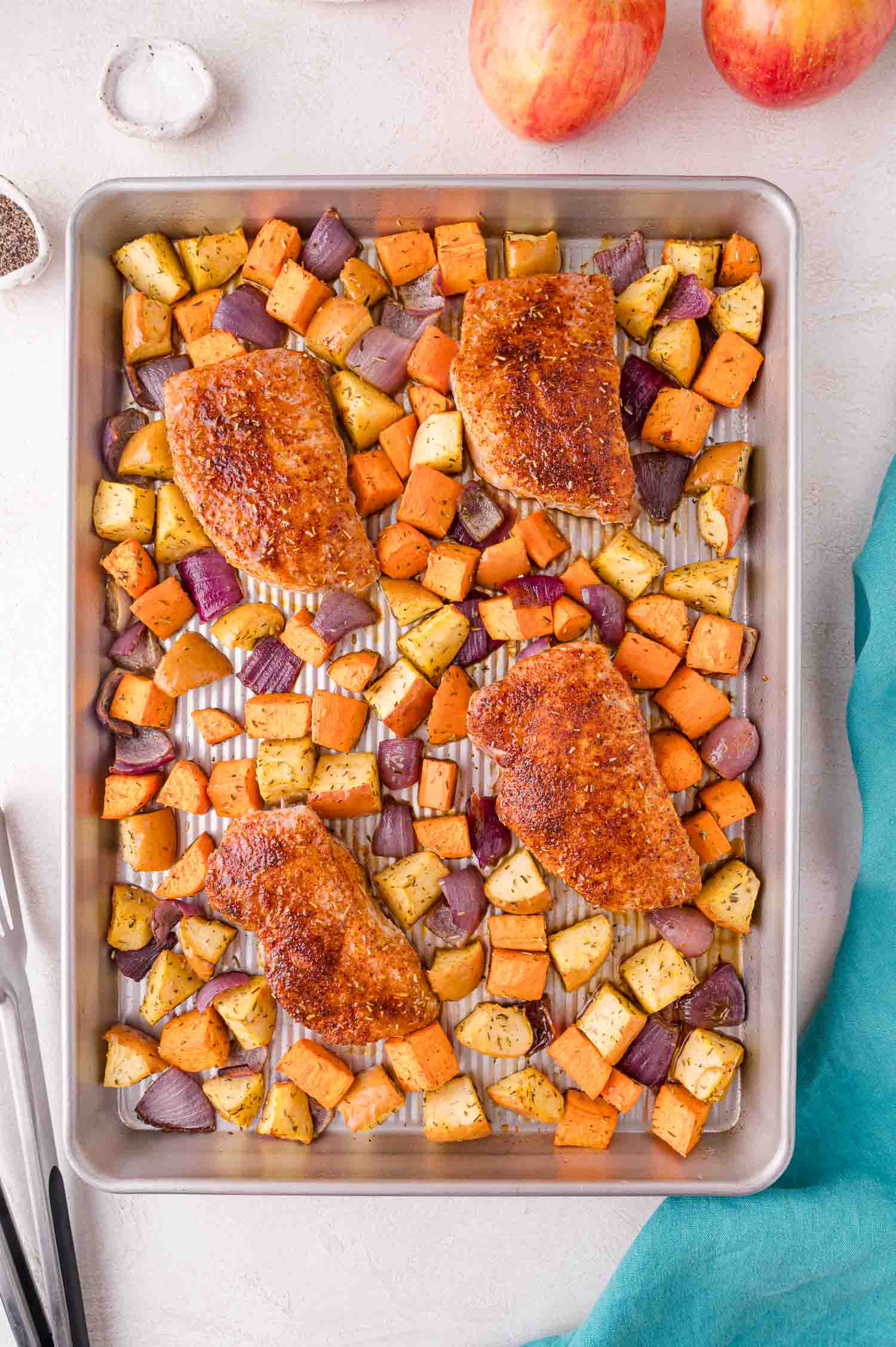 Baked pork chops with diced sweet potatoes, apples, and red onions arranged on a sheet pan, ready to serve.