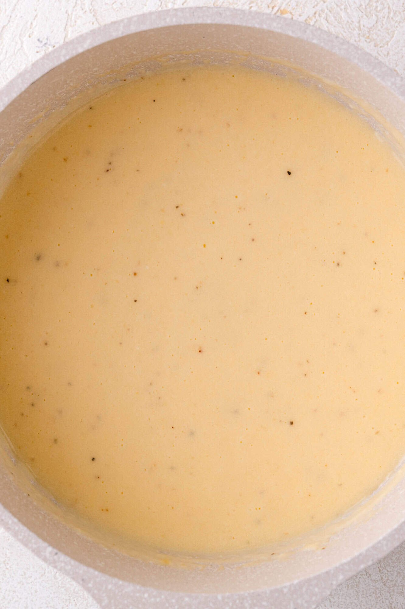 A pot filled with creamy, light yellow cheese sauce with small specks of seasoning visible throughout.