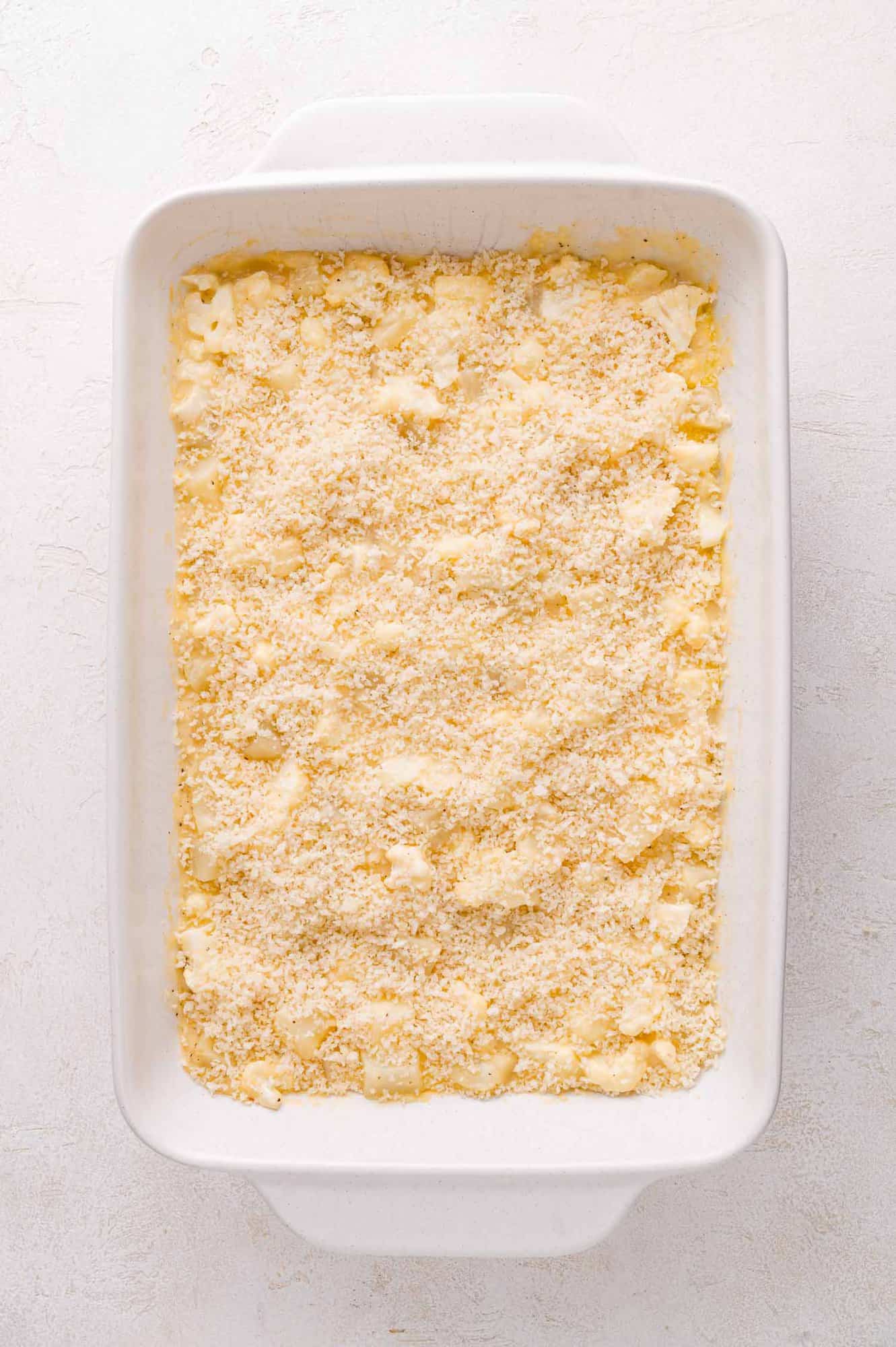 A rectangular white baking dish filled with an unbaked casserole topped with breadcrumbs.