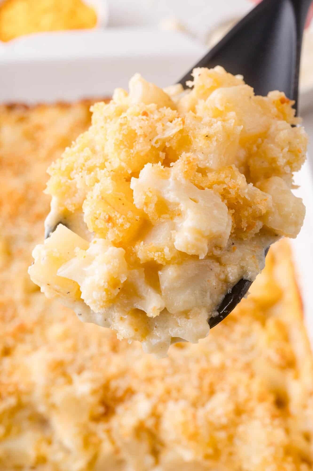 A close-up of a spoonful of cauliflower and potato casserole with a golden breadcrumb topping.