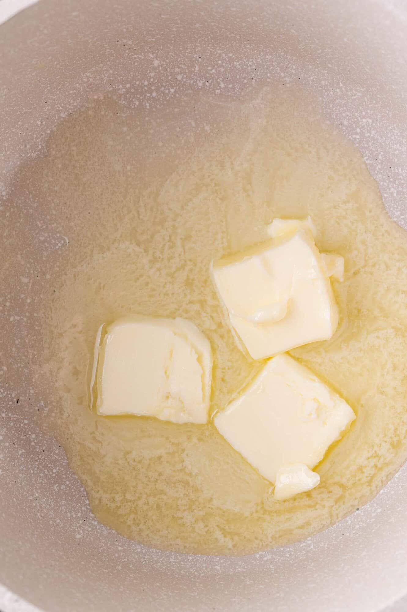Three partially melted cubes of butter in a white saucepan.