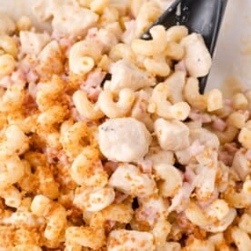 Close-up of creamy pasta with chunks of chicken, diced ham, breadcrumbs, and a black serving spoon.