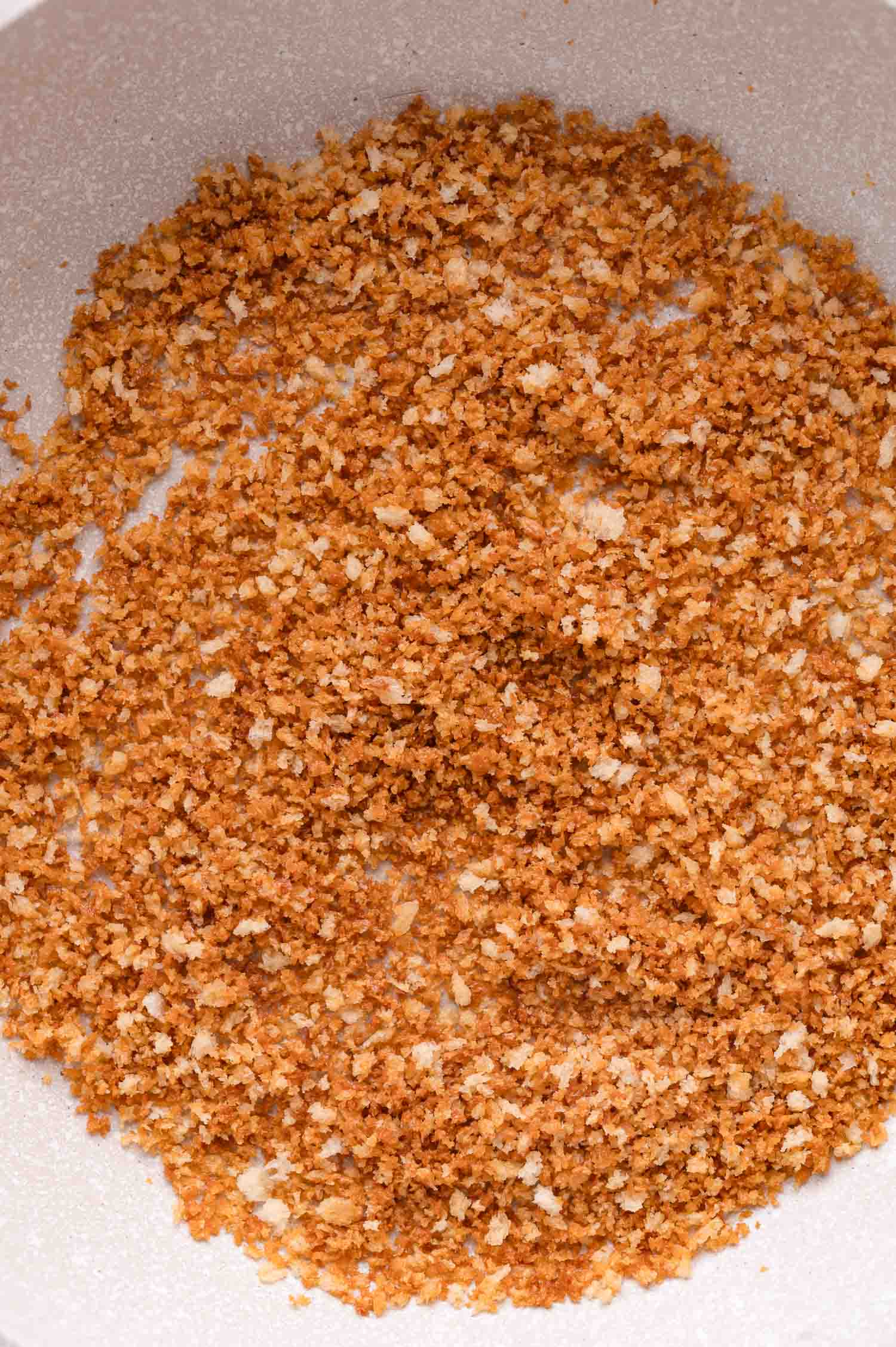 Close-up of golden-brown toasted breadcrumbs in a white pan.
