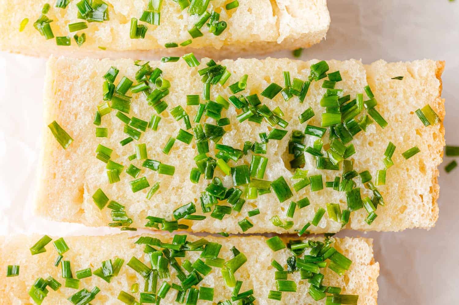 Slices of bread topped with chopped fresh chives and coarse salt, arranged on a light surface.