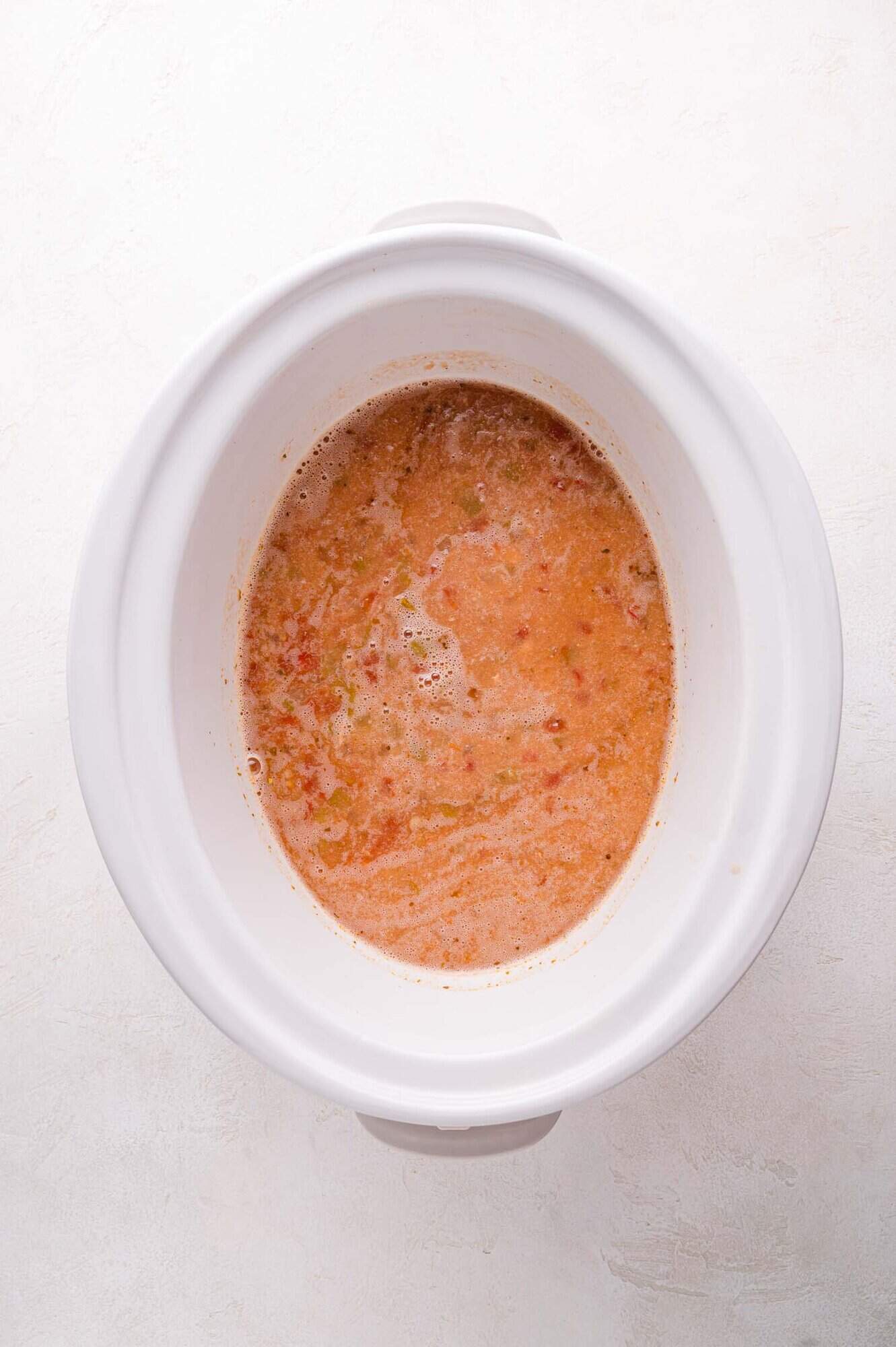 Slow cooker containing a blended mixture of ingredients, on a light surface.