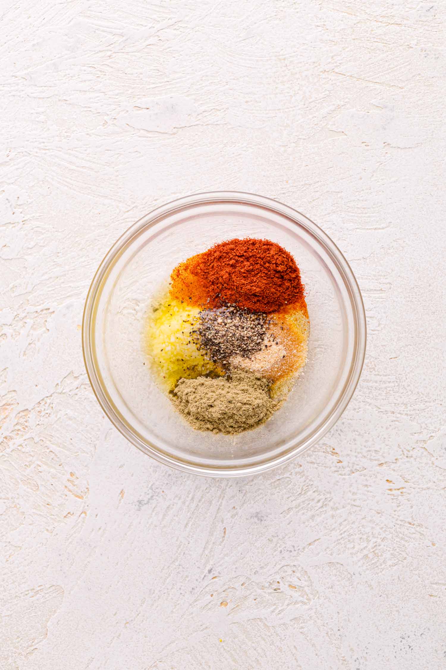 A glass bowl containing ground spices, arranged in separate piles on a textured white surface.