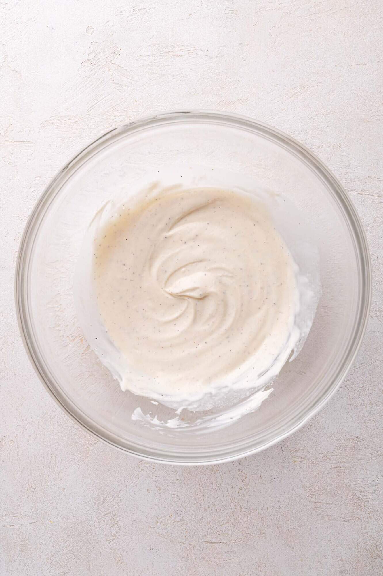 A glass bowl containing a smooth, creamy white mixture with visible specks, placed on a light-colored surface.