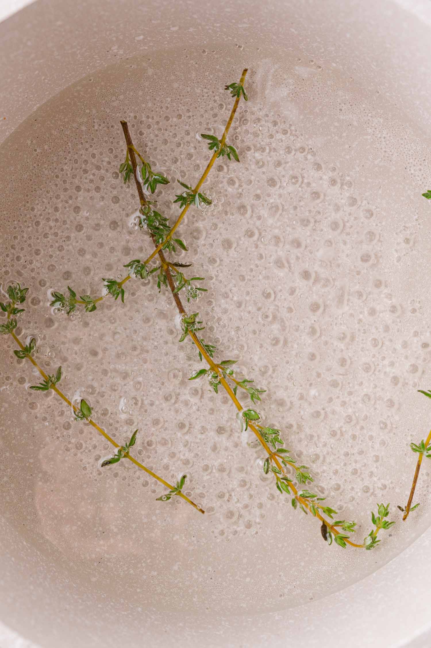 Two sprigs of fresh thyme floating in a pot of boiling simple syrup.