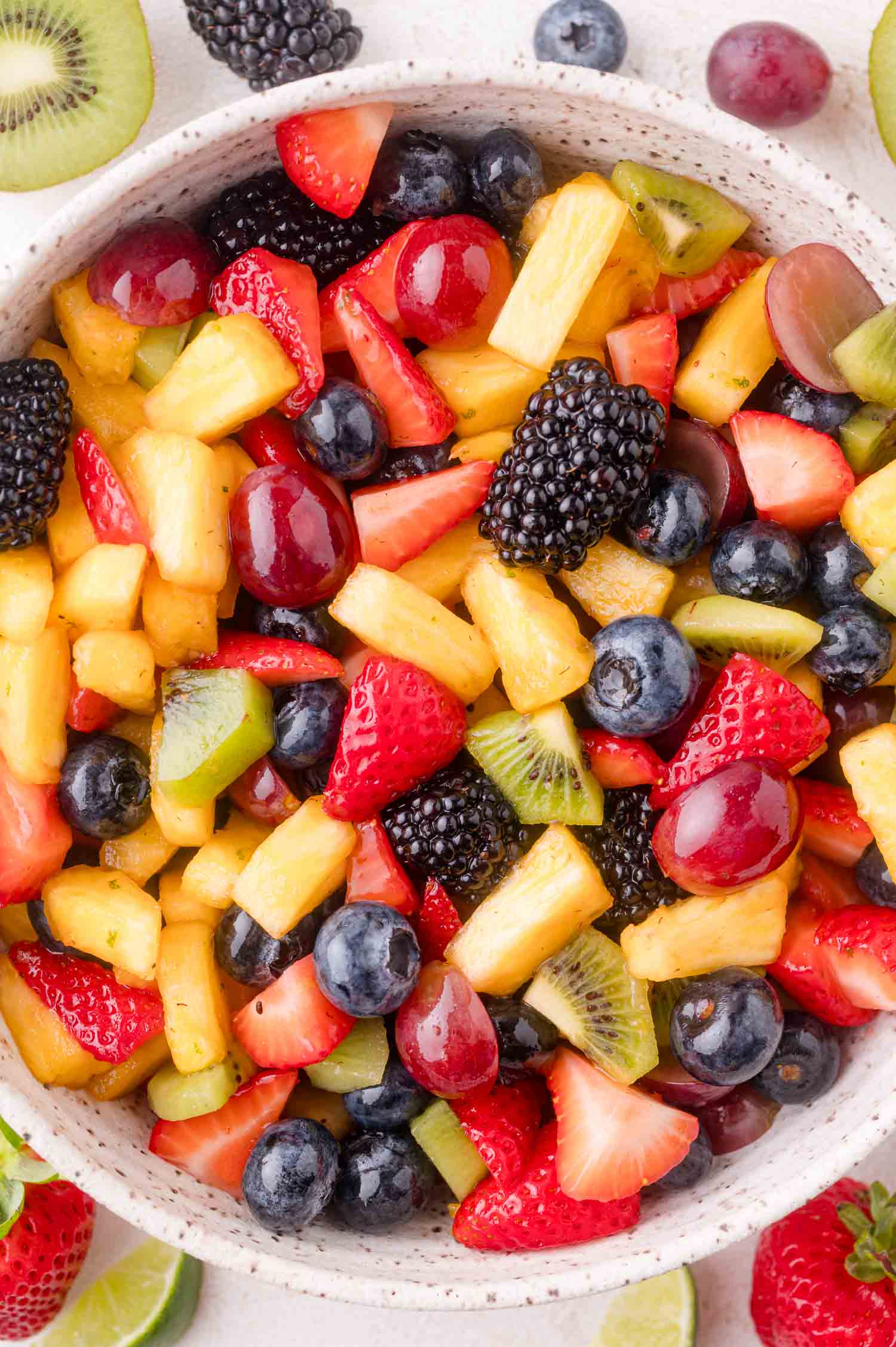 A bowl filled with a colorful mix of fresh fruit pieces, including strawberries, kiwi, pineapple, blackberries, grapes, and blueberries.