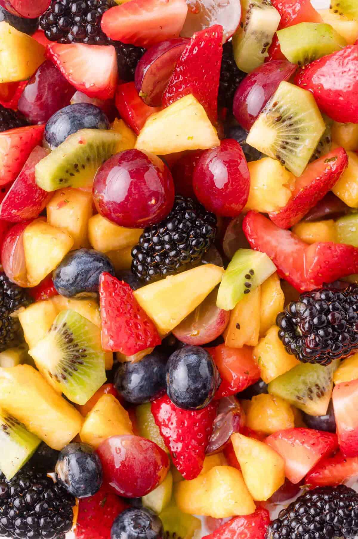 A close-up of a mixed fruit salad containing strawberries, blueberries, blackberries, grapes, kiwi, and pineapple.