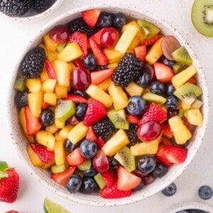 A bowl filled with a mixed fruit salad containing strawberries, blueberries, blackberries, pineapple, kiwi, grapes, and pieces of other assorted fruits.