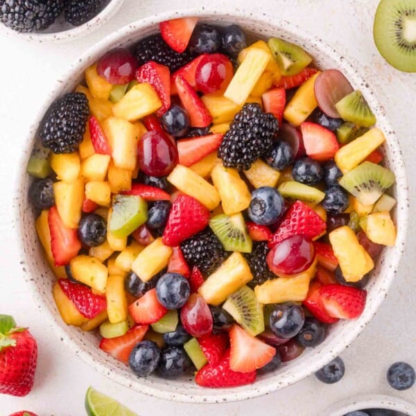 A bowl filled with a mixed fruit salad containing strawberries, blueberries, blackberries, pineapple, kiwi, grapes, and pieces of other assorted fruits.