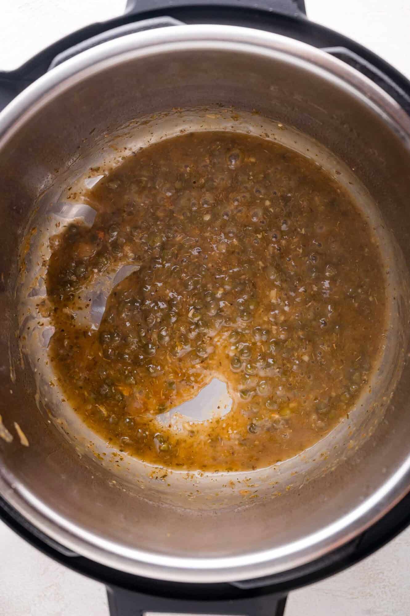 A close-up view of a brown, bubbling liquid sauce inside a stainless steel pot or pressure cooker.