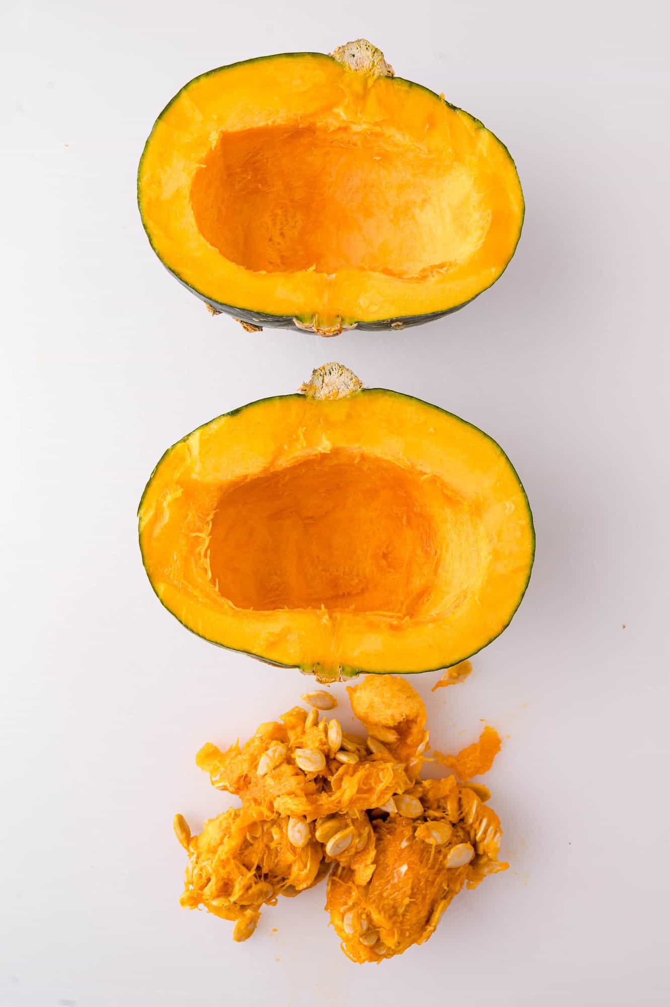 A kabocha squash cut in half with seeds and fibrous pulp removed, displayed on a white surface.
