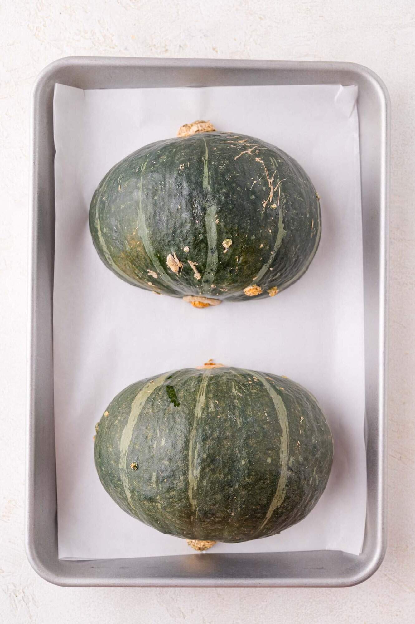 Two whole green squash halves placed side by side on a parchment-lined baking tray.
