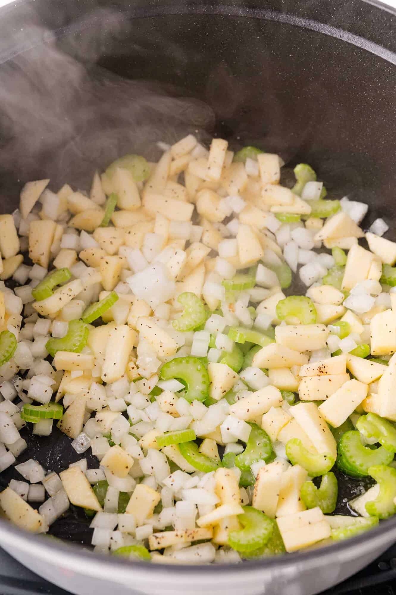 Diced onions, celery, and apples sautéing in a pan with visible steam rising.