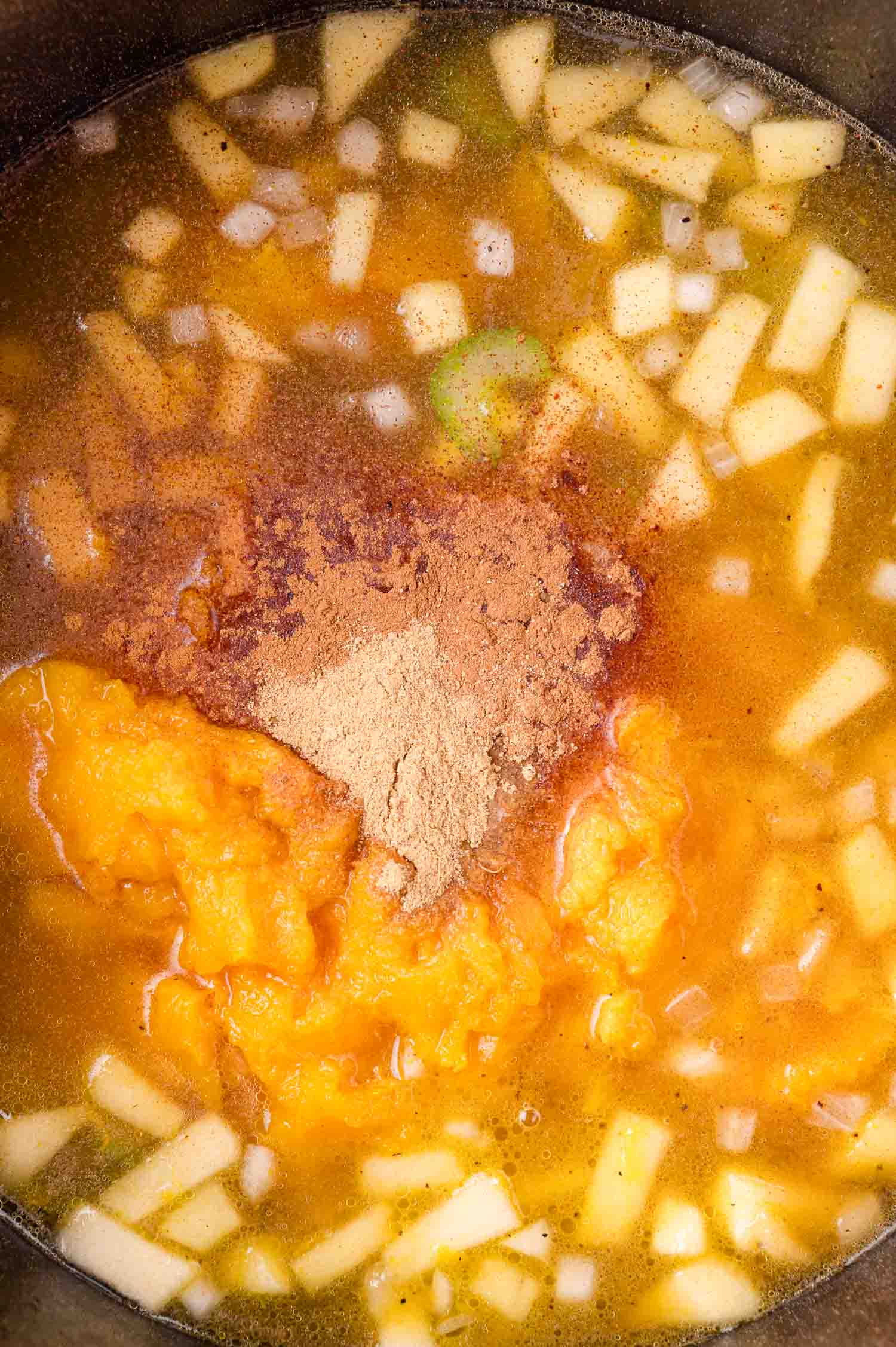 Chopped onions, apples, cooked squash, broth, and spices in a pot, ready to be mixed and cooked.