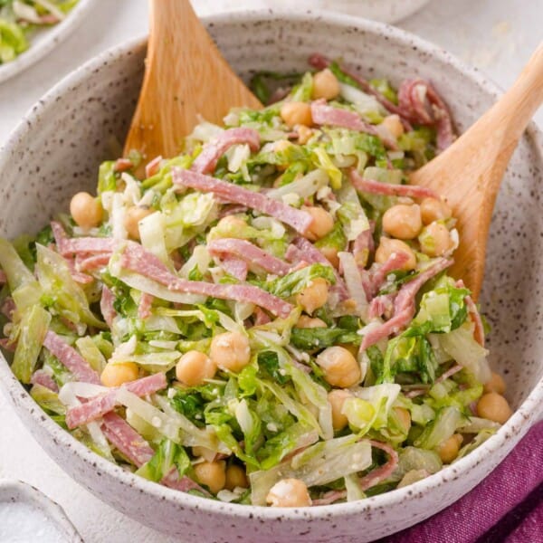 A bowl of La Scala chopped salad with lettuce, chickpeas, sliced salami, and cheese, mixed and served with two wooden salad utensils.