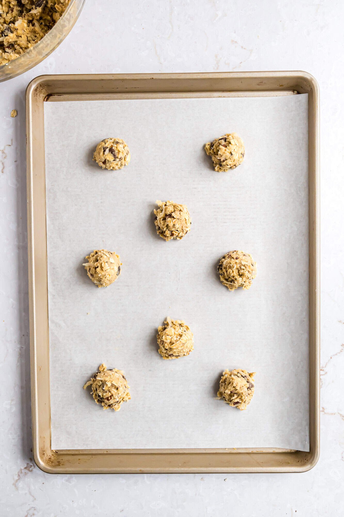 A baking sheet lined with parchment paper holds eight evenly spaced scoops of unbaked cookie dough.