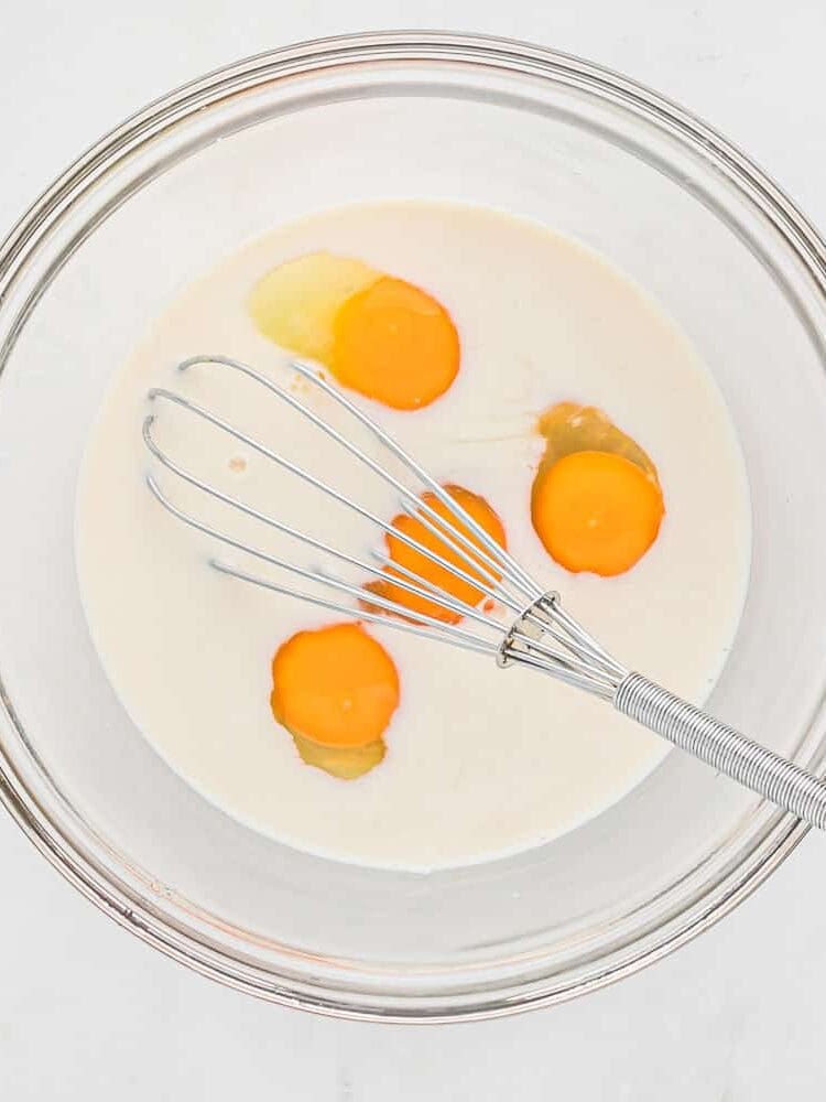Eggs and milk in a bowl with a whisk.