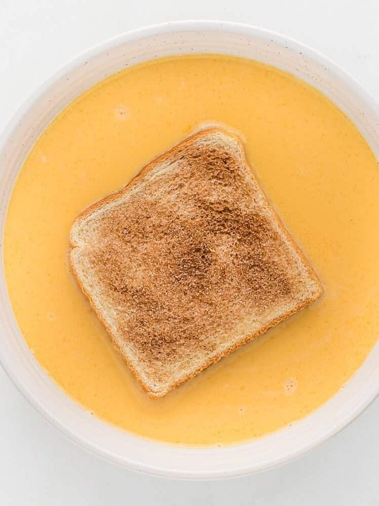 A bread slice dipped in a bowl of egg mixture.