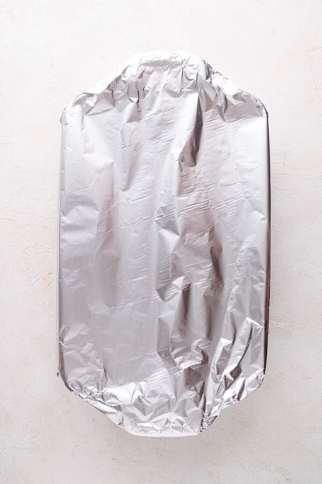 A rectangular baking dish covered with a sheet of crinkled aluminum foil on a light-colored surface.