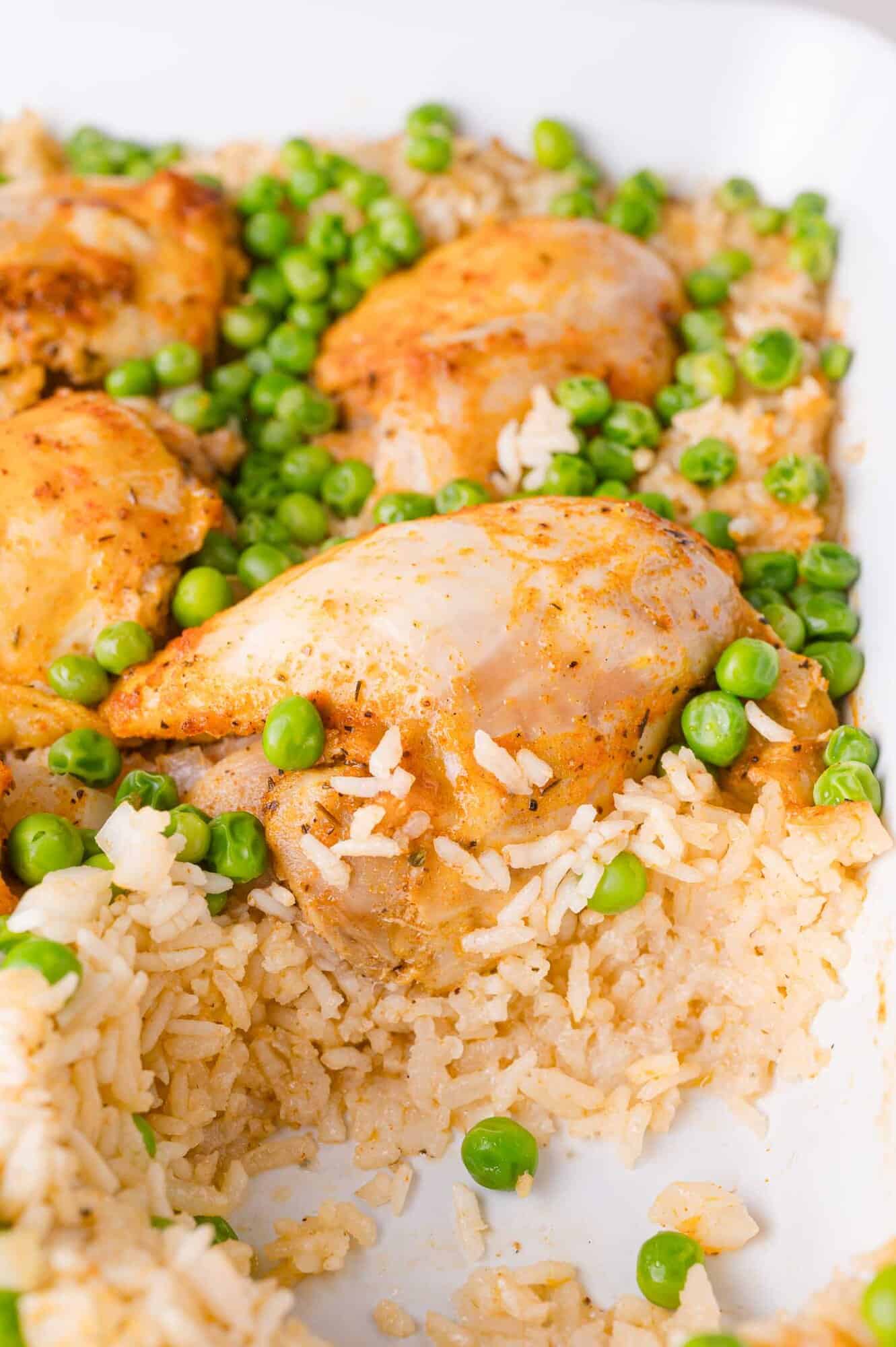 Baked chicken thighs served with white rice and green peas in a white dish.