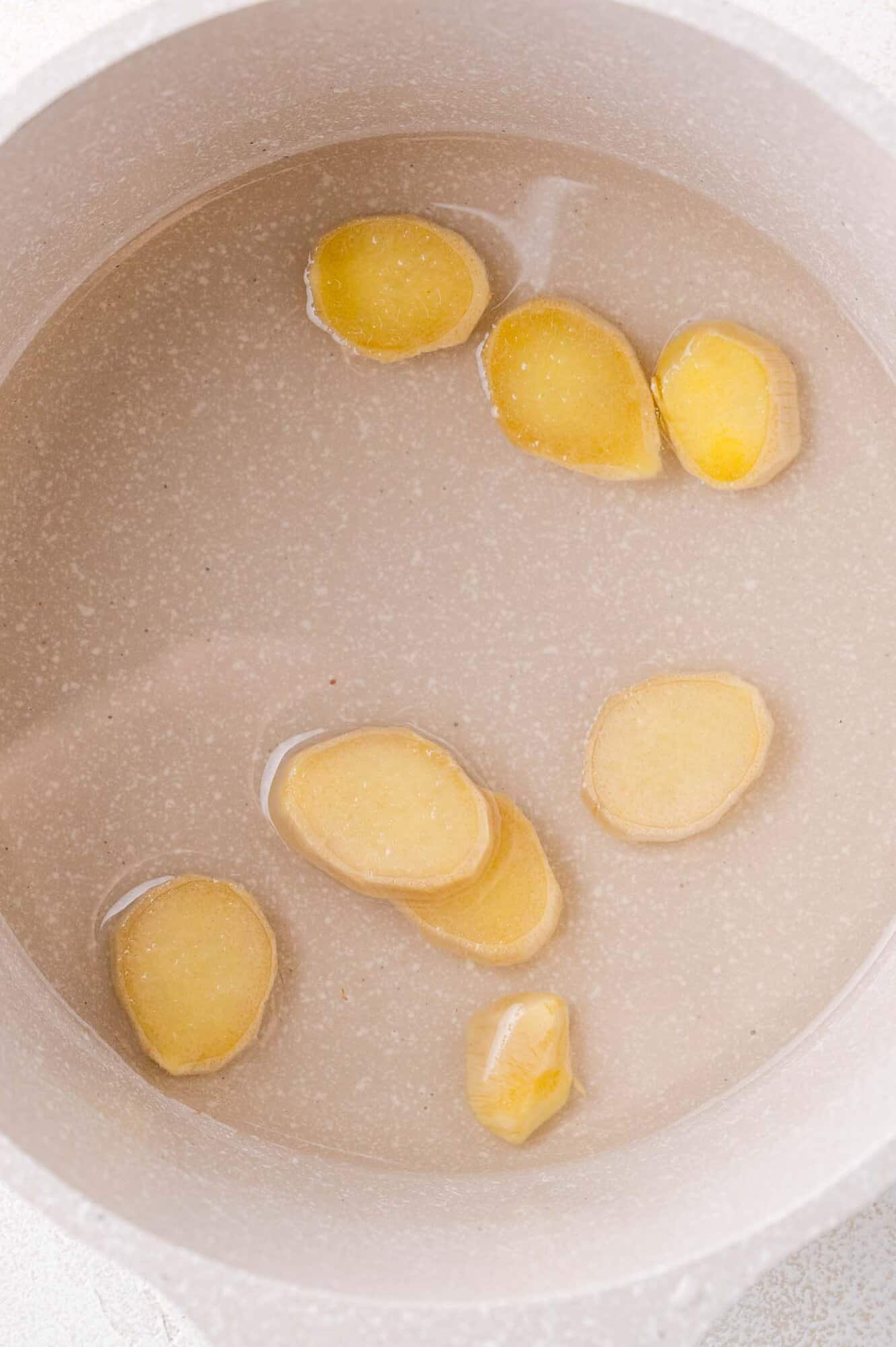 Sliced ginger pieces floating in a pot of simple syrup.