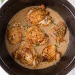 Braised chicken thighs in a creamy gravy, garnished with chopped herbs, served in a black Dutch oven.