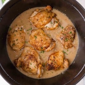 Braised chicken thighs in a creamy gravy, garnished with chopped herbs, served in a black Dutch oven.