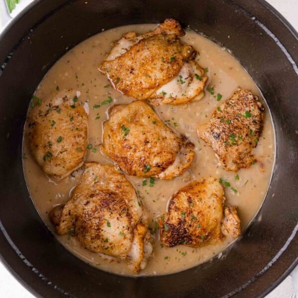 Braised chicken thighs in a creamy gravy, garnished with chopped herbs, served in a black Dutch oven.