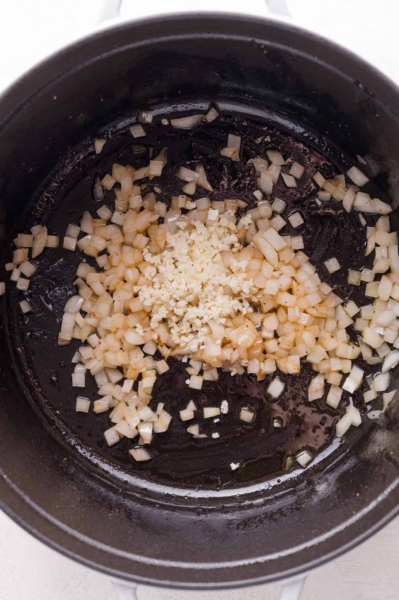 Diced onions and minced garlic sautéing in a black pot.